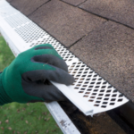 Hand installing a white gutter guard on a roof, emphasizing gutter maintenance and debris prevention for effective water flow.