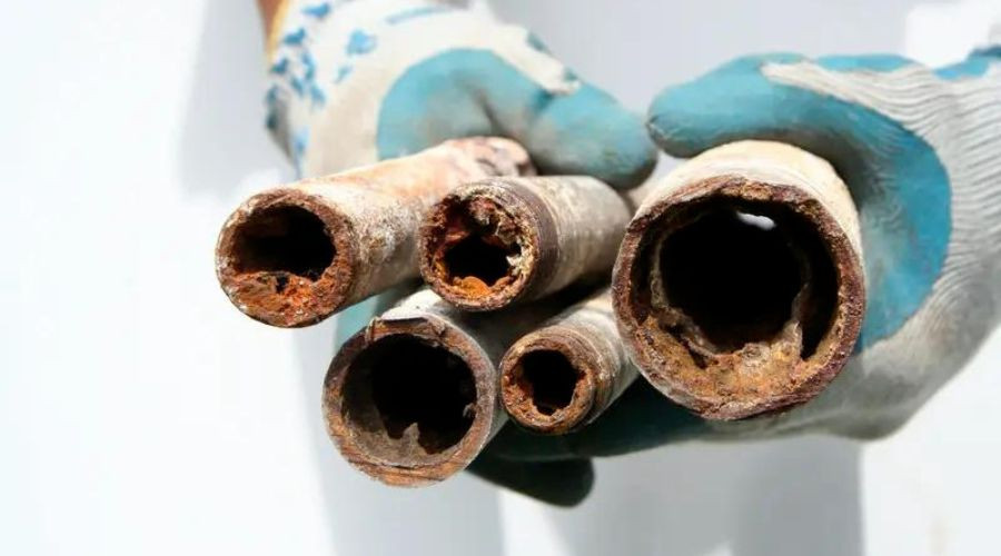 Rusty plumbing pipes held by a gloved hand, illustrating the need for repiping in outdated plumbing systems.