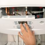 Hand adjusting the control panel of a boiler, illustrating routine maintenance for optimal heating efficiency and energy savings.